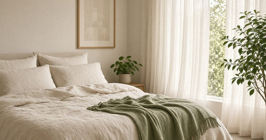 Calm bedroom with cream linen bedding, a sage-green throw and soft morning light